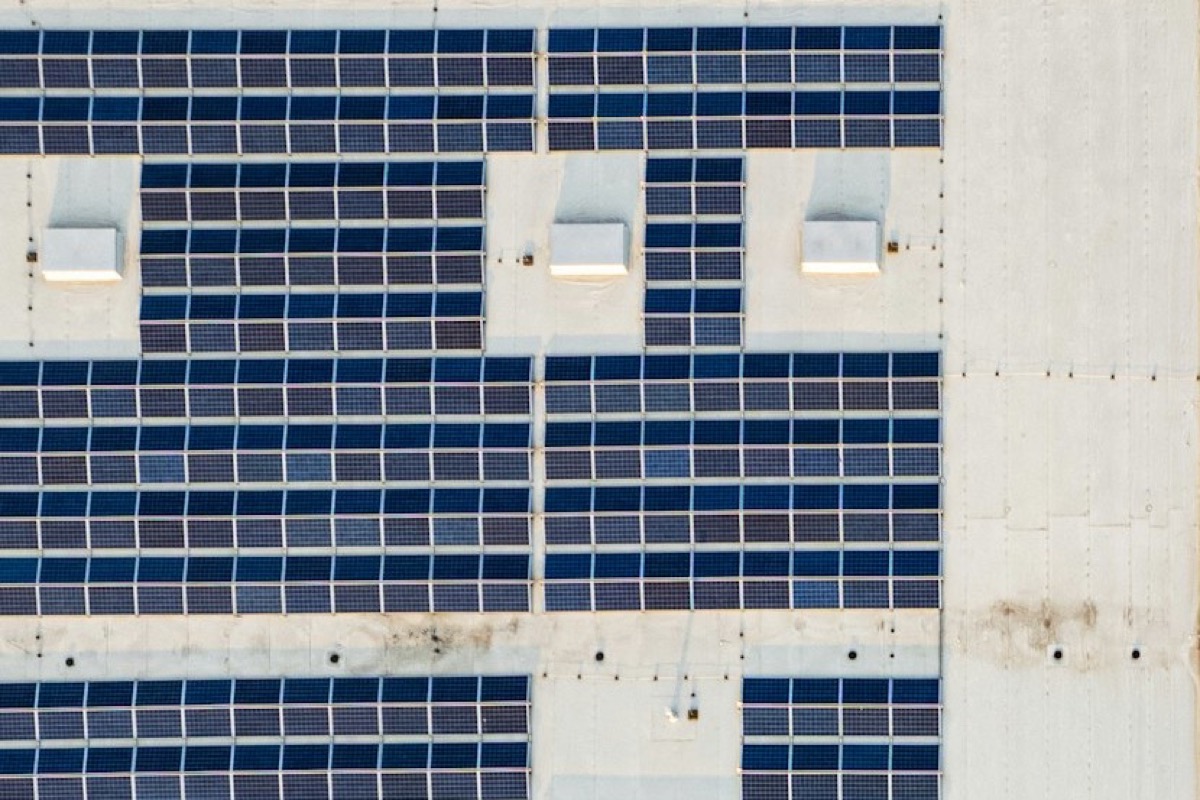 Rows of solar panels on a flat warehouse roof, seen from above