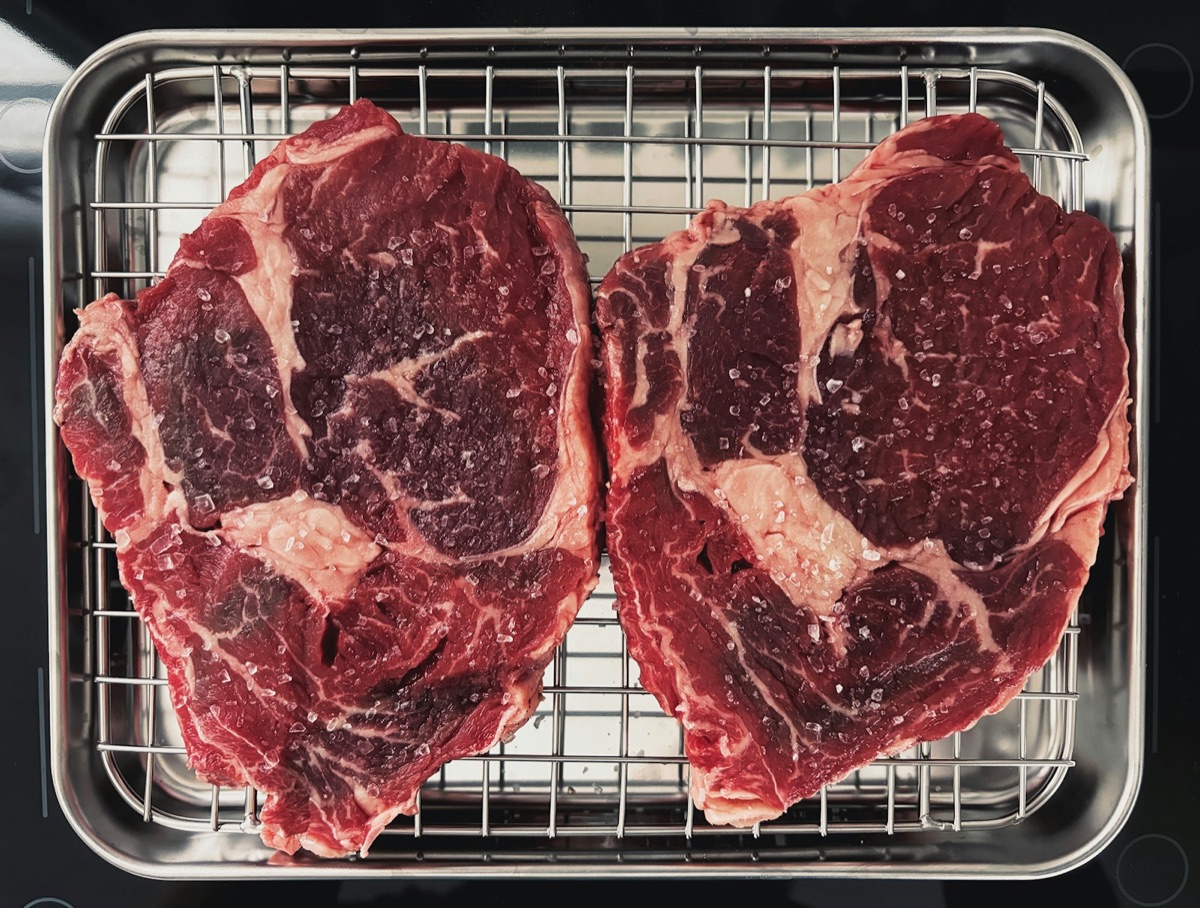 Two raw ribeye steaks on a rack